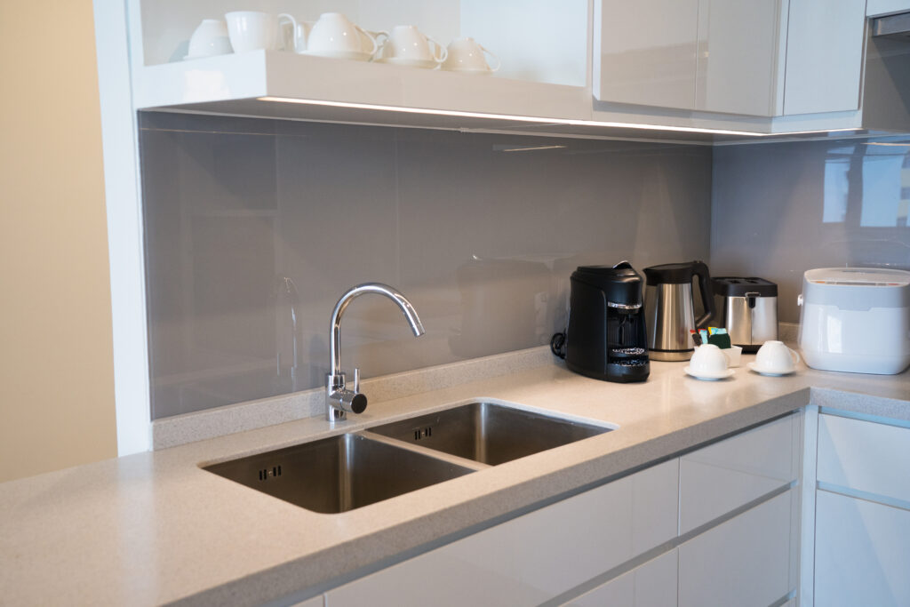 Modern grey glass kitchen backsplash behind a stainless steel double sink.