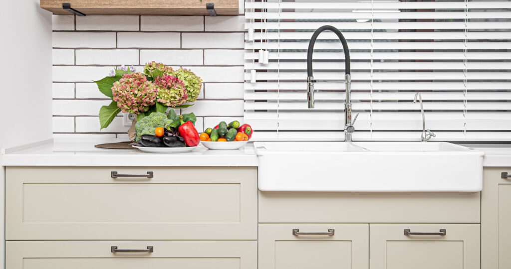 White subway tile backsplash with dark grout behind a farmhouse sink and vegetables.